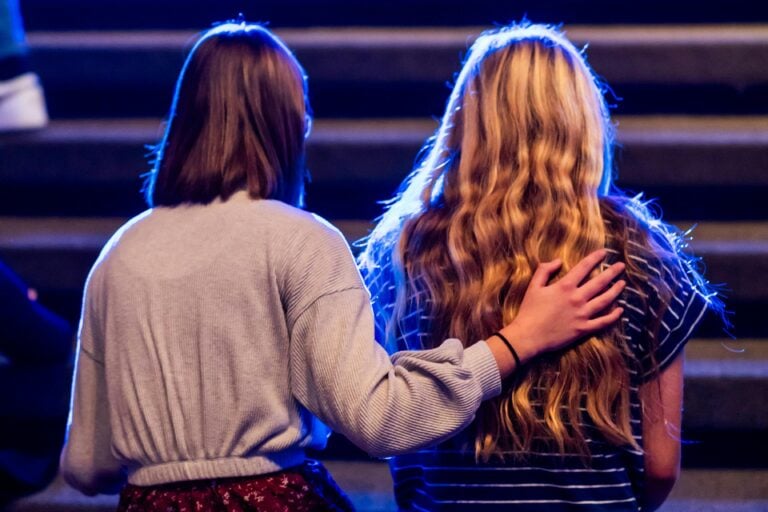 Two women kneeling. One woman has her hand on the back of the other woman.