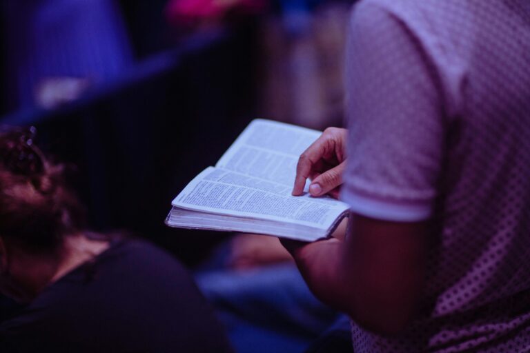 Man reading the bible in church next to a woman praying.